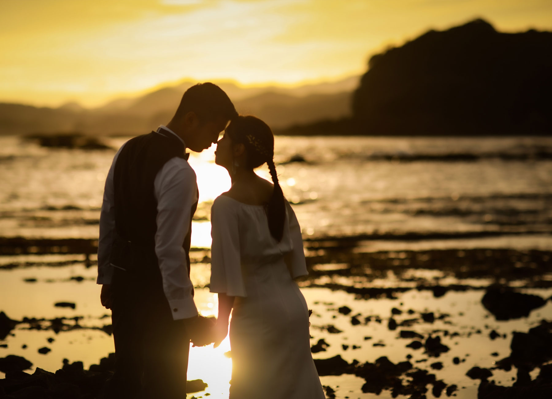 伊豆の海辺で夕日を背景に寄り添う新郎新婦